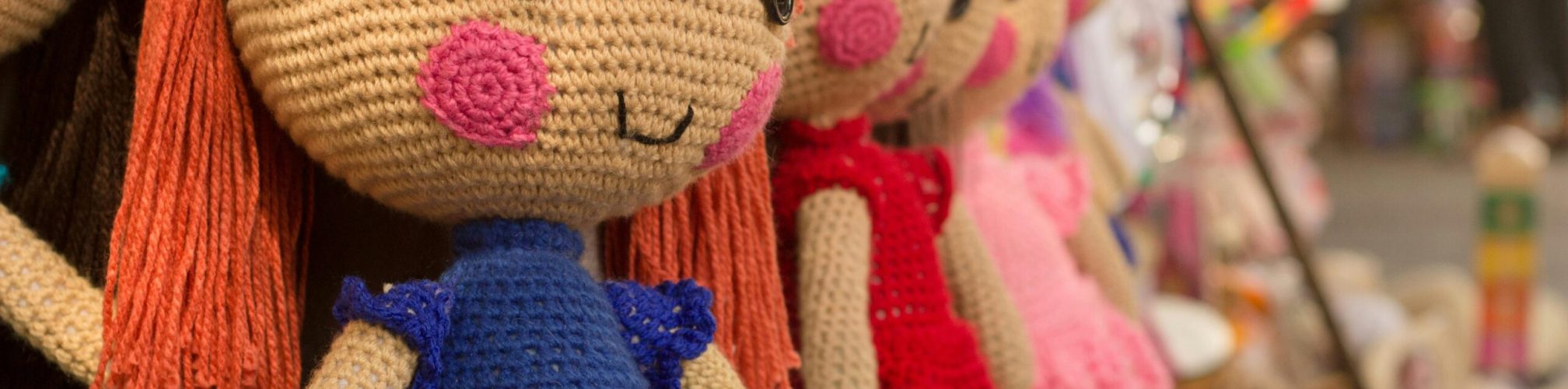 Charming crocheted dolls in bright clothes hang at a market stall.